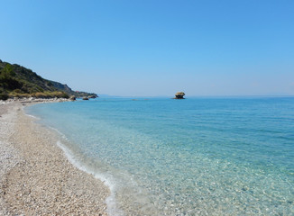 Fototapeta na wymiar An empty white stone beach with transparent turquoise sea and rocks in Cephalonia or Kefalonia in Greece.