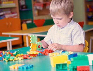 Little boy in the children's room plays in the constructor on the table.