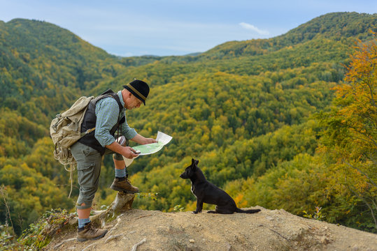 An older traveler with a dog and map in the mountains is looking for the right tourist route.