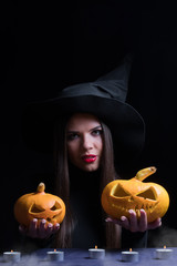 Halloween Witch with a magic Pumpkin. Beautiful young woman in witches hat and costume holding carved pumpkin. Halloween art design