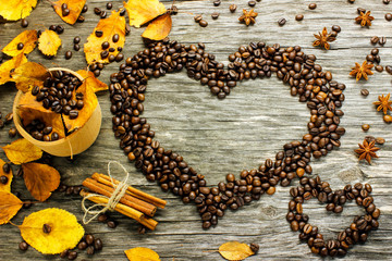 a heart of coffee beans strewn with autumn yellow leaves, anise and cinnamon on a wooden surface.