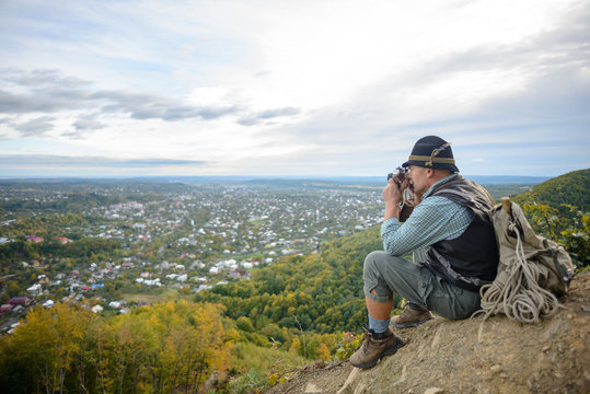 An Elderly Old Man Resting On The Top Of The Mountain Enjoys A Panoramic View Of The City. Senior Traveler Picks Up In The Mountains.
