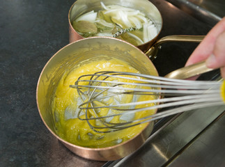 A whisk mixing golden organic olive oil and white flour in a metal kitchen pan, in an industrial kitchen setting. Step by step cake recipe.
