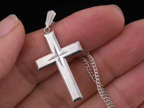 Silver cross and chain in hand, Christian jewelry symbol.