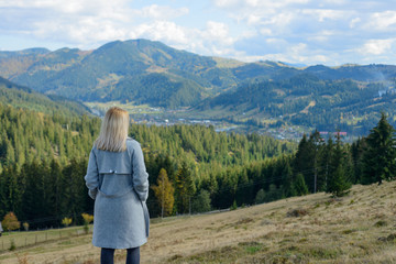 A young blond girl is standing on top and enjoying the panorama of a mountain town.
