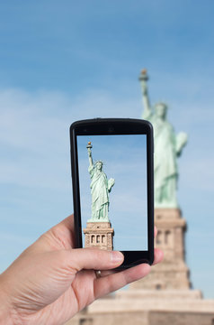 Man hand holding smartphone capturing a picture of the Statue of Liberty
