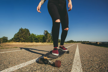 A beautiful, sexy blond hipster with blue hair in a tattoo is riding a longboard.