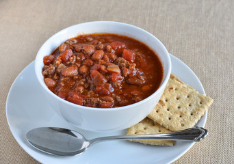 Bowl of hot chili with saltine crackers and spoon