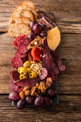 Cheese and meat appetizer selection. Prosciutto di Parma, salami, bread sticks, baguette slices, olives, grapes and nuts on rustic wooden background.