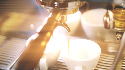 Close up of a coffee machine pouring coffee into two white cups.