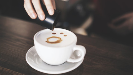 Close up of woman barista s hands drawing a butterfly on coffee surface in a white cup. Coffee shop concept.