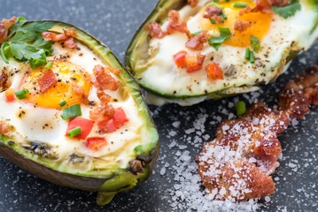Eggs baked in avocado with bacon, red paprika and chive.