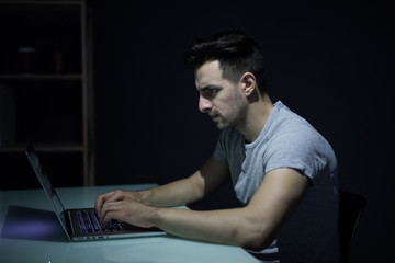 Male programmer working on desktop computer at white desk in office in dark