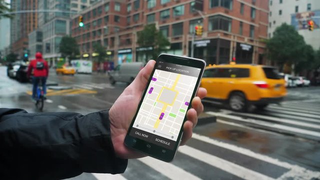 A man uses his smartphone to observe ride sharing traffic patterns on an interactive map in a fictional city on a rainy day.	 	