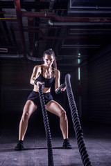 Battle ropes session. Attractive young fit and toned sportswoman working out in fitness  training gym