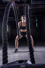 Battle ropes session. Attractive young fit and toned sportswoman working out in fitness  training...