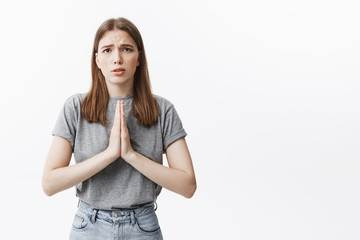Fototapeta premium Please, forgive me. Young beautiful european girl with dark healthy hair and brown eyes in grey clothes looking in casmera with guilty expression, trying to ask for forgiveness from mother.