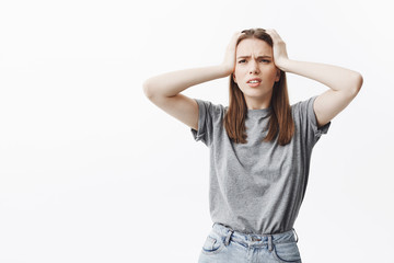 Good-looking young caucasian female student with dark hair in casual clothes squeezing head with hands, looking aside, suffering from terrible headache after party last night.