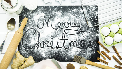 inscription Happy Christmas on a black board sprinkled with flour among the ingredients for baking ginger biscuits