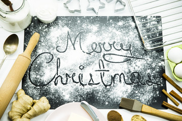 inscription Happy Christmas on a black board sprinkled with flour among the ingredients for baking ginger biscuits