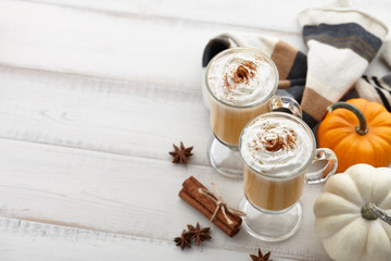 Fall pumpkin spice latte with whipped cream and cinnamon, ornamental pumpkins and warm woolen scarf on white wooden background, copyspace