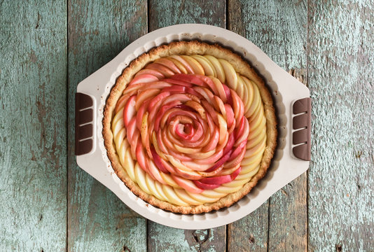 Exquisite homemade dessert. Pie with rose made of apples in baking dish on blue background