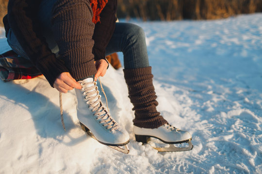 Cropped image of a woman putting ice skates on. Woman lacing ice skates at the edge of a frozen lake.