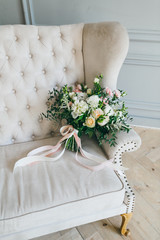 Rustic wedding bouquet with creamy roses and white carnations on a luxury cream sofa. Close-up. Side view