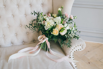 Rustic wedding bouquet with creamy roses and white carnations on a luxury cream sofa. Close-up....