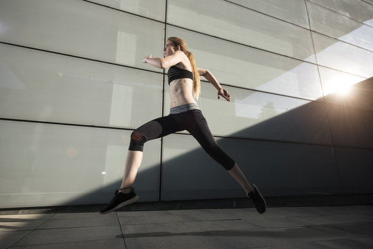 Sportswoman running and looking forward at street in sunlight.