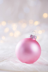 Pink Christmas ball on white lace on light and warm bokeh background