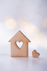 Wooden house with hole in the form of heart with little heart on light bokeh background