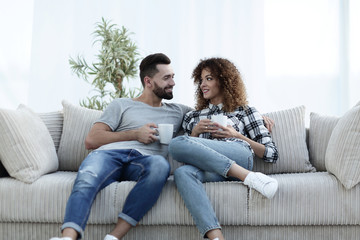 Obraz premium Beautiful couple holding a cup of drink while sitting on the couch at home