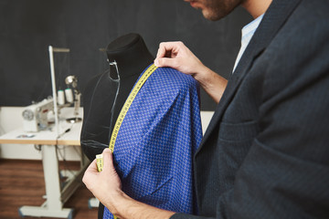 Naklejka premium Close up detail of talented professional young caucasian male designer working on new dress for spring collection, checking sizes with measuring tape, spending day in his workshop