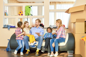 Family sitting on sofa, relocation. Parents with children, cardboard boxes.