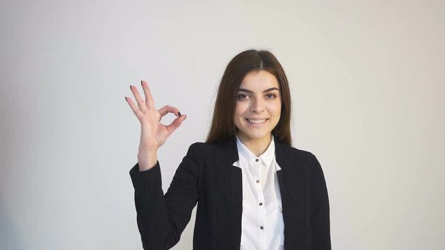 Beautiful caucasian woman, in white blouse and black jacket, showing OK sign in the white background, isolated slowmotion