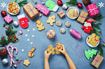 Christmas background with gifts, cookies, Christmas decoration and children's hands holding gingerbred cookies