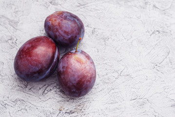Three Round Ripe Plums on gray rustoc background. Autumn fruits.