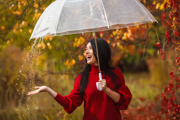 Beautiful woman holding umbrella in the rain and smiling. Autumn background. Cheerful young girl having fun at the rain in the fall time.