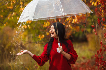 Beautiful woman holding umbrella in the rain and smiling. Autumn background. Cheerful young girl...