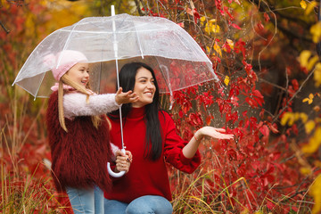 Cheerful mother and her little daughter having fun together in the autumn background under the...