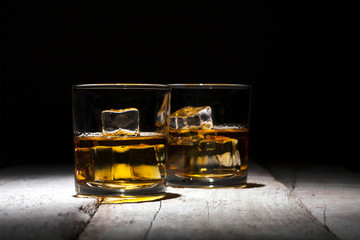 Two glasses of whiskey with ice cubes served on white wooden planks.