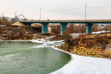 Car bridge over the ice-free river. Boiling water, river rapids, snow on the banks