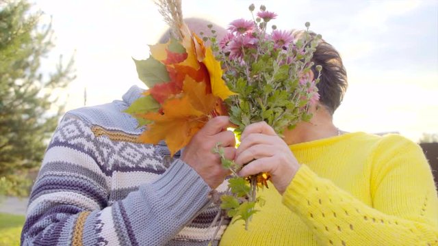 Senior couple is kissing and closing their face with a bouquet of flowers