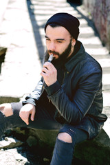 Bearded young man smokes an electronic cigarette or vape