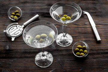 Make martini cocktails. Glass with beverage, olives and utensils on dark wooden background top view