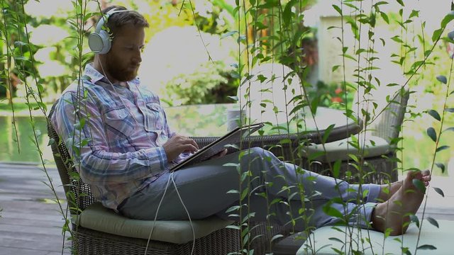 Handsome man sitting in the garden and using modern notebook
