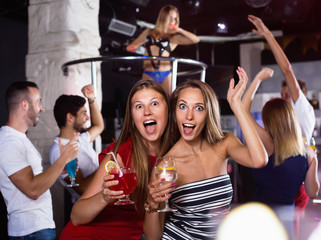 smiling women dancing in the night club with drinks in the hand