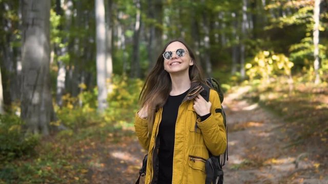 Caucasian female tourist, in yellow jacket and black sunglasses, enjoys the forest, slowmotion on sunny fall day