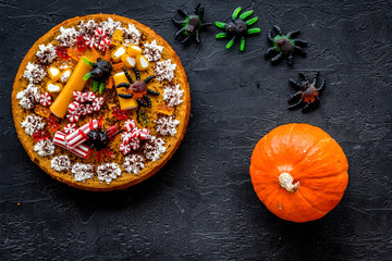 Fototapeta na wymiar Gummy spiders crawls toward pie for halloween on black background top view
